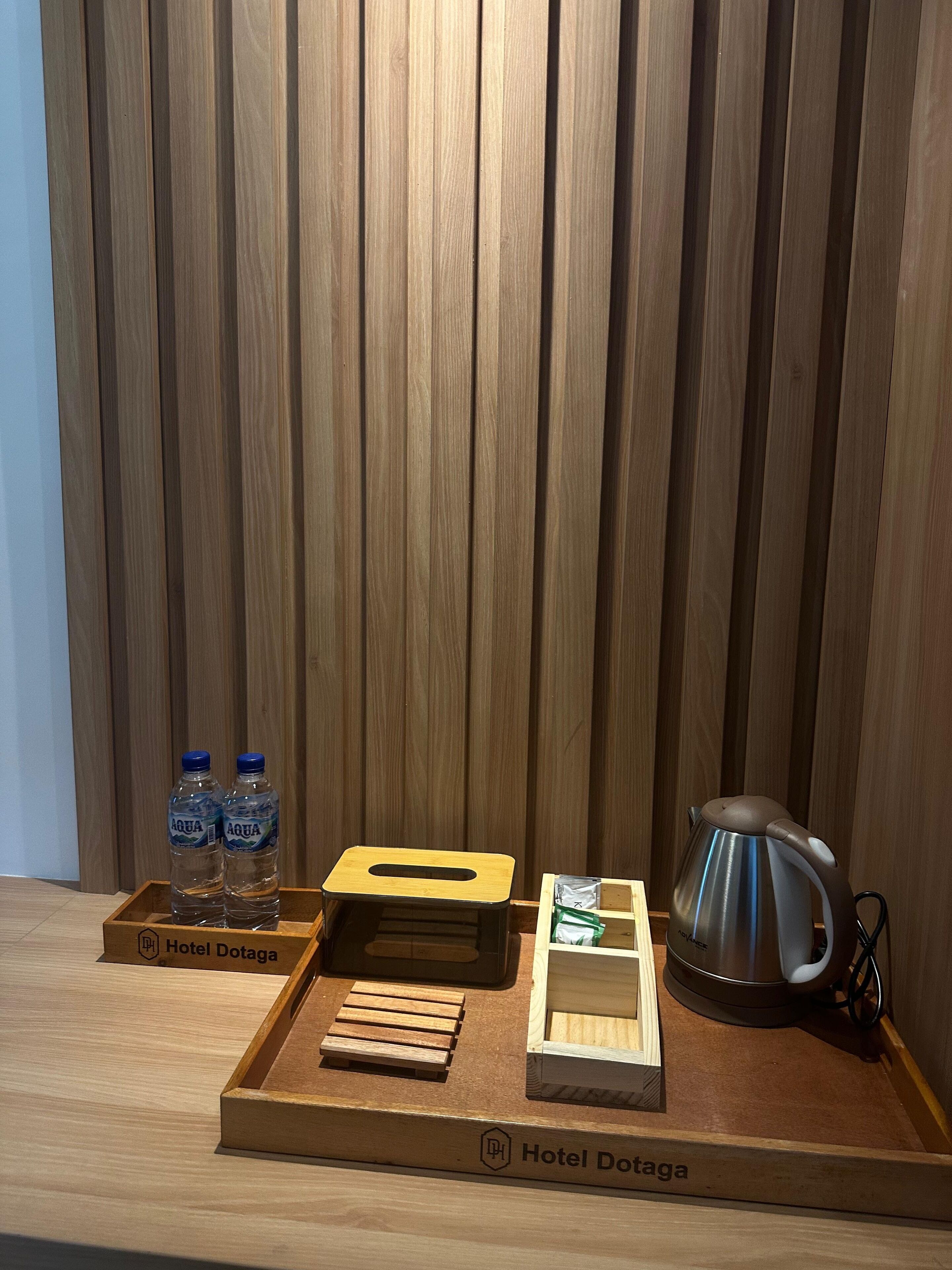 Una bandeja de madera con una tetera, dos botellas de agua y una caja de madera con la etiqueta 'Hotel Dotaga'.