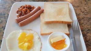 Un piatto colazione con uova, pane tostato, salsicce e fagioli.