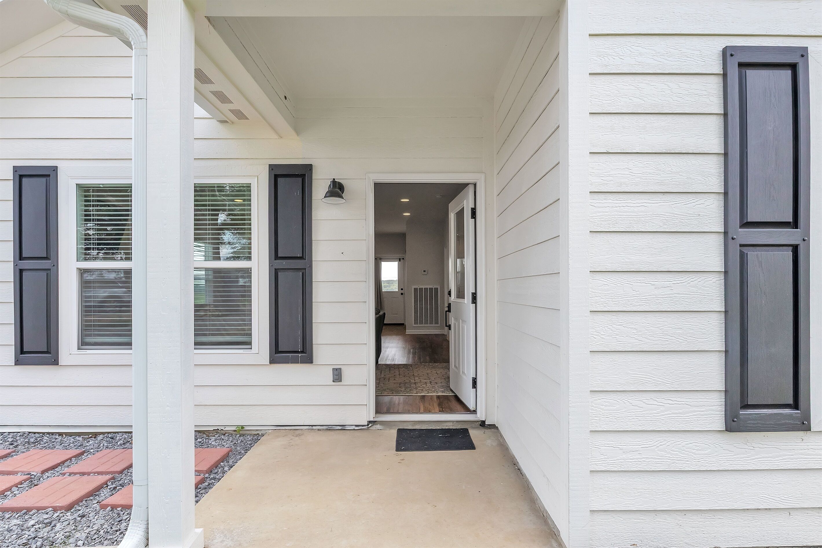 Une maison dotée d’un porche abrité, d’une porte visible donnant sur l’intérieur et d’un petit espace extérieur agrémenté d’un paillasson.
