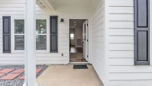 Ein Haus mit überdachter Veranda, einer sichtbaren Tür, die in den Innenbereich führt, und einer kleinen Außenfläche mit Fußmatte.