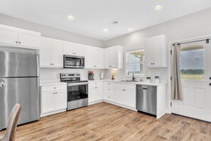 A modern kitchen with white cabinets, stainless steel appliances, and a wooden floor.