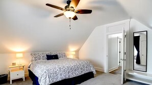 A bedroom with a bed, a ceiling fan, two bedside lamps, a door, and a mirror. - Hot Tub~Gym~5 Min to Mass Ave~Backyard Retreat~Indianapolis (Indianapolis)