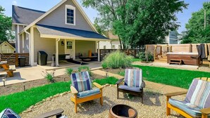 A house with a covered porch, outdoor seating area with chairs and a table, and a well-maintained lawn. - Hot Tub~Gym~5 Min to Mass Ave~Backyard Retreat~Indianapolis (Indianapolis)