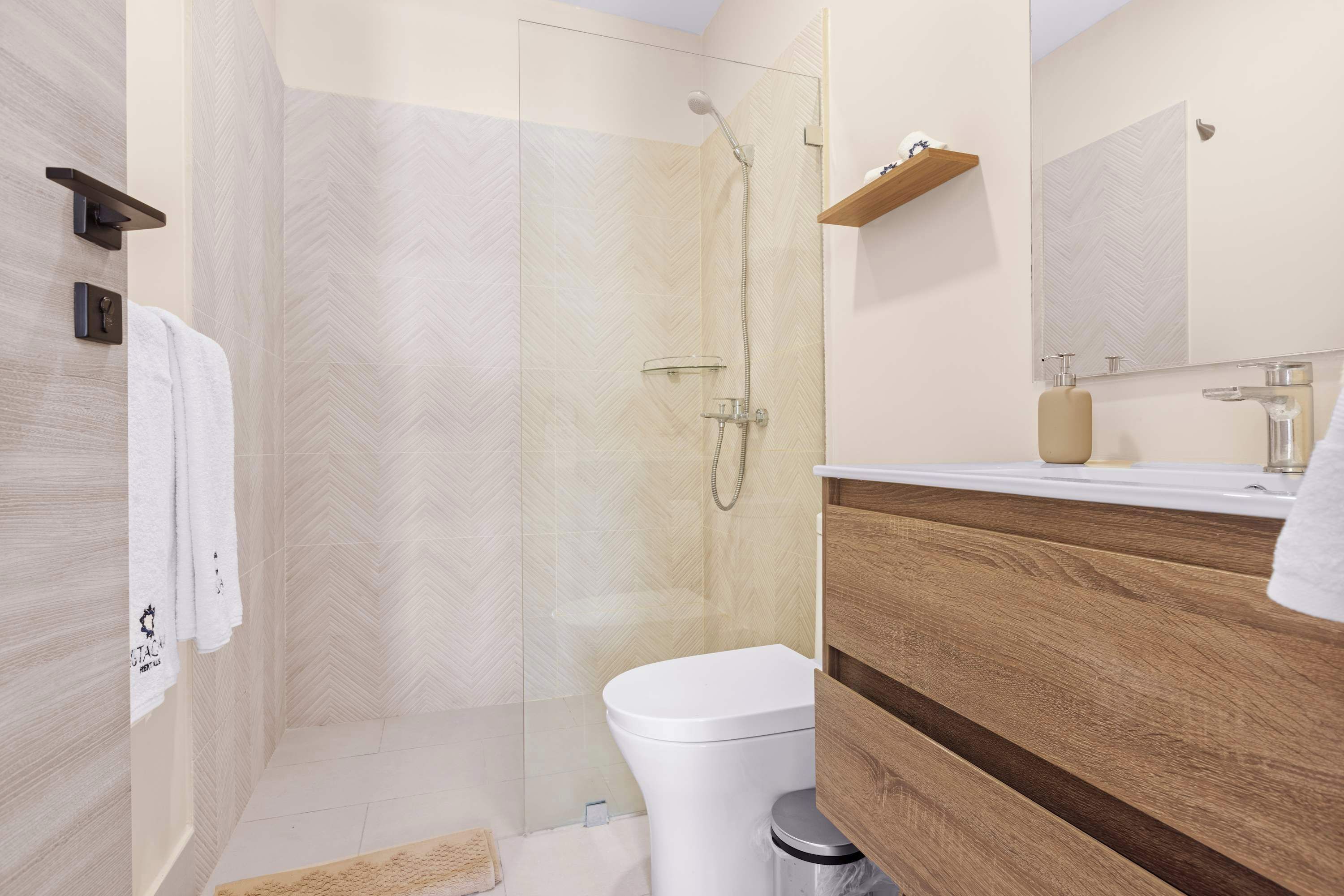 Un baño moderno con ducha de vidrio, tocador de madera y un espejo grande.