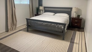 A bedroom with a bed, two bedside tables, a nightstand, a window with curtains, and a ceiling light. - Haddock Heights (Williams Lake)