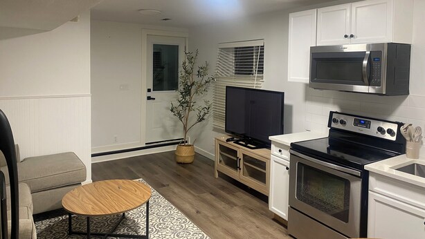 A compact kitchen with white cabinets, a microwave, a stove, and a television. - Haddock Heights (Williams Lake)