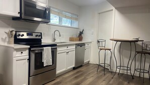 A modern kitchen with white cabinetry, stainless steel appliances, a wooden floor, and a small dining area with stools. - Haddock Heights (Williams Lake)