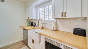 Une cuisine moderne avec des meubles blancs, un plan de travail en bois, un lave-vaisselle encastré et un grille-pain.