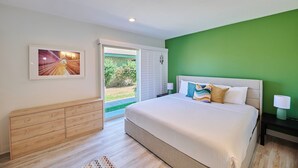 Une chambre à coucher avec un lit, une commode, une table de chevet, une lampe, un tableau encadré et un mur vert.