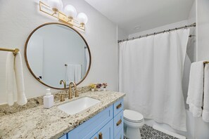 A bathroom with a round mirror, a sink, blue cabinets, a toilet, and a shower curtain. - Scottsdale Escape - 3 Bed Condo in Old Town Scottsdale! (Scottsdale)