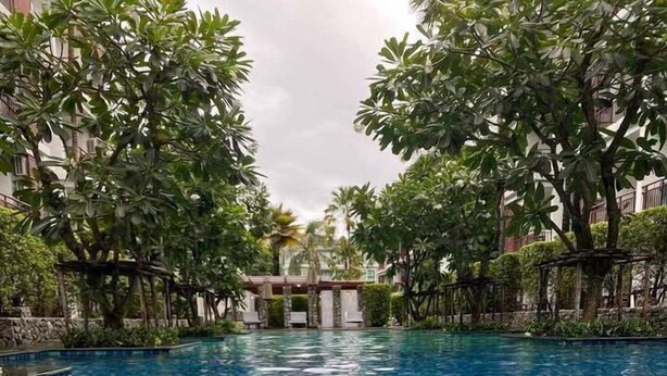 Una piscina con agua azul cristalina, rodeada de exuberante vegetación y un puente de piedra al fondo.