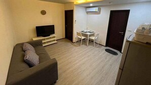 Un espacio habitable compacto con sofá, televisión, una pequeña mesa de comedor con sillas y una zona de kitchenette.
