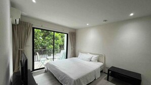 Un dormitorio moderno con una cama grande, un televisor, una banca y un balcón con cortinas.