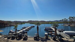 A marina with boats docked, a bridge in the background, and palm trees along the water.