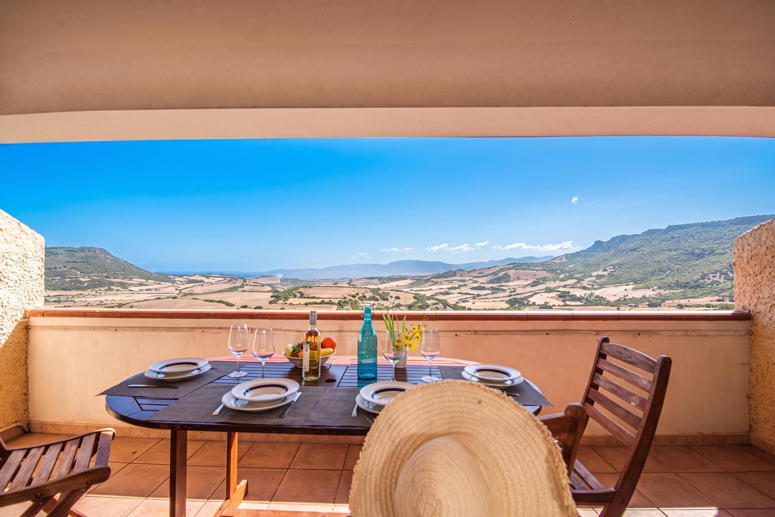 A balcony with a table set for two, overlooking a scenic landscape.