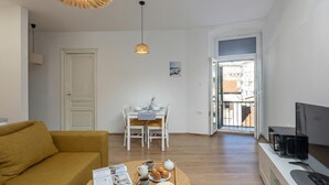 A living room with a sofa, a dining table with chairs, a TV, and a tray with food and drinks. - Anna | 4-Bedroom City Apartment (Rijeka)