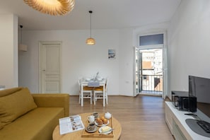 A living room with a sofa, a dining table with chairs, a TV, and a tray with food and drinks.