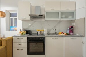 Eine moderne Küche mit eingebautem Ofen, einem Herd und einer Mikrowelle. Über der Spüle ist ein Fenster, und auf der Arbeitsfläche steht eine Obstschale.