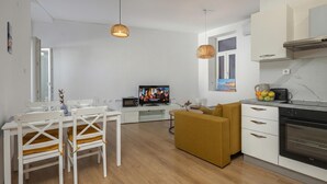 A modern kitchen with a microwave, oven, and a dining area with a white table and chairs. - Anna | 4-Bedroom City Apartment (Rijeka)