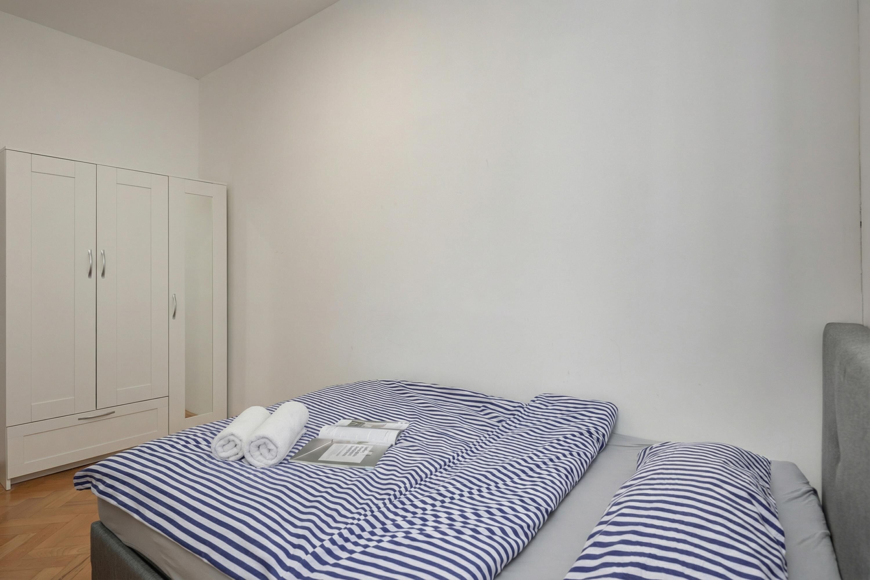 Um quarto com cama, almofadas, guarda-roupa e mesa de cabeceira.