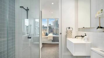 A modern bathroom with a glass shower enclosure, a white sink with a mirror, and a view of a cityscape through an open door.