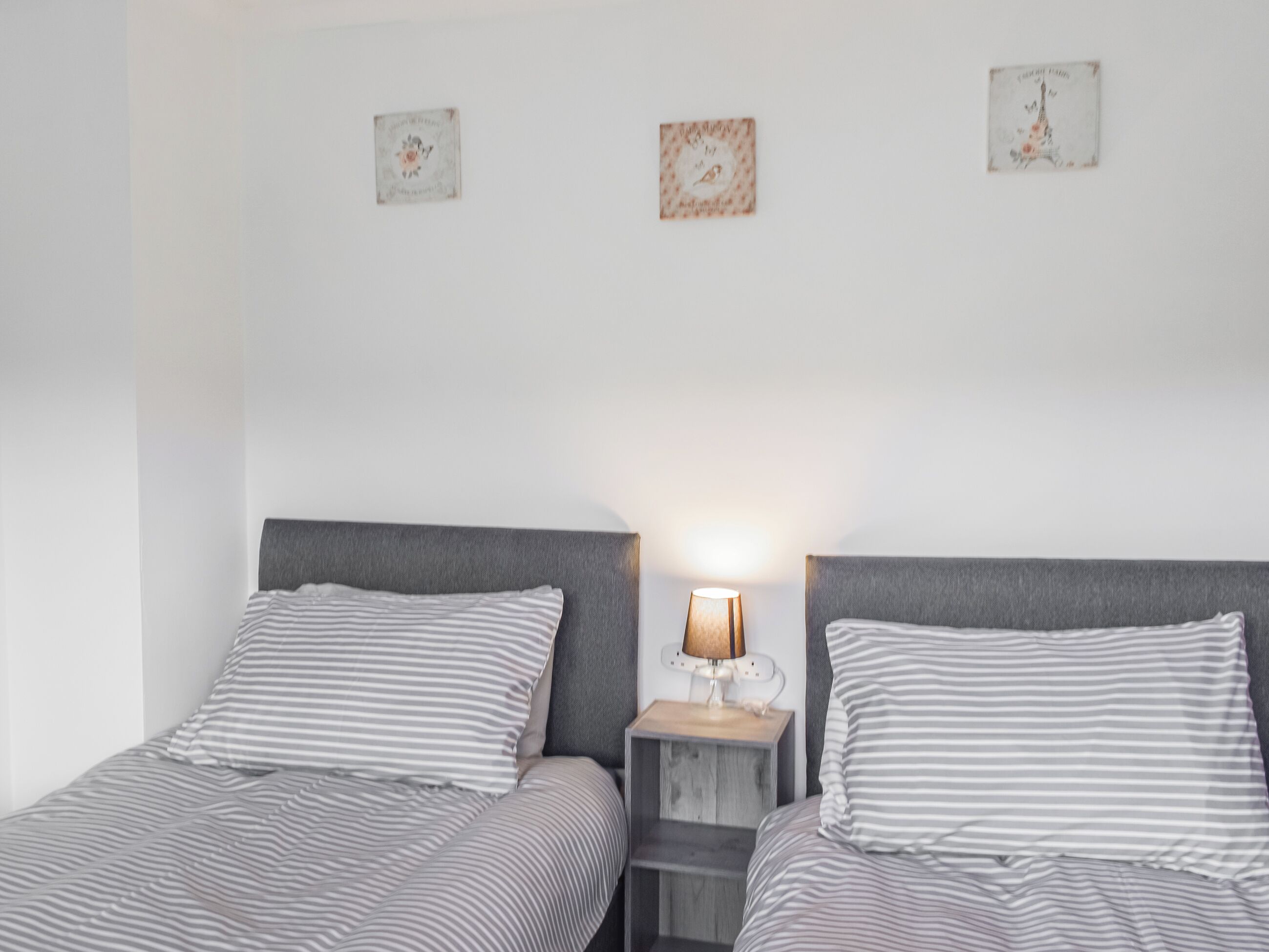 A double bed with striped bedding, a bedside table with a lamp, and two small decorative items on the wall.
