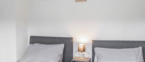 A double bed with striped bedding, a bedside table with a lamp, and two small decorative items on the wall.