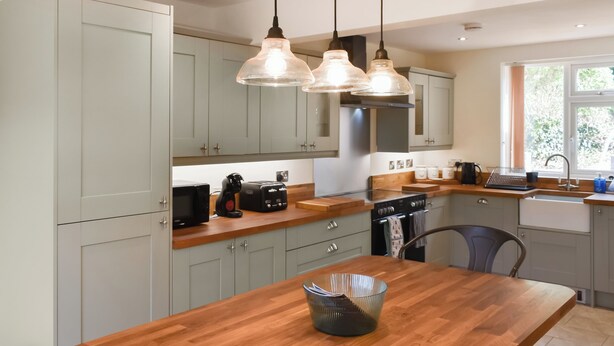 A modern kitchen with light grey cabinets, a wooden countertop, and pendant lighting. - 3 bedroom accommodation in Cinderford (Cinderford)