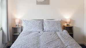 A bedroom with a bed, two bedside lamps, a wall-mounted artwork, and a window with curtains. - 3 bedroom accommodation in Cinderford (Cinderford)