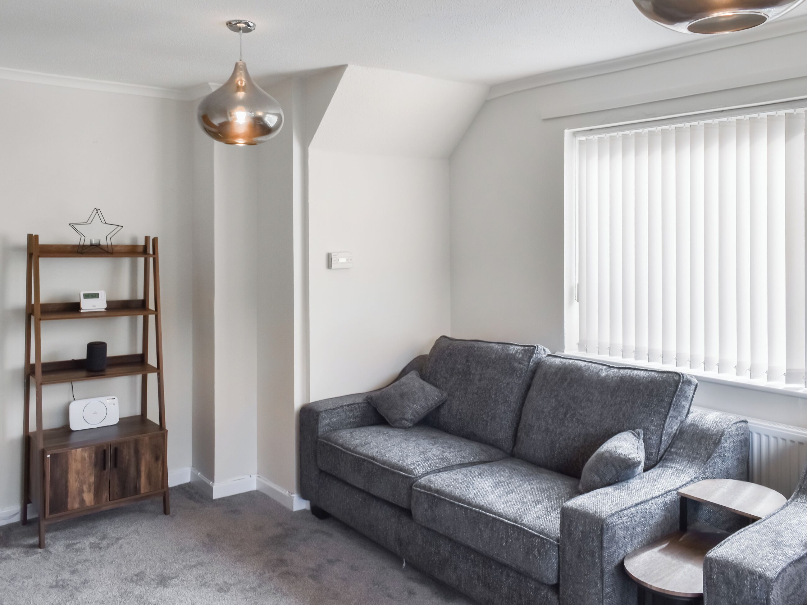 A modern living room with a grey sofa, a wooden side table, a hanging pendant light, and a star-shaped decoration on a shelf.