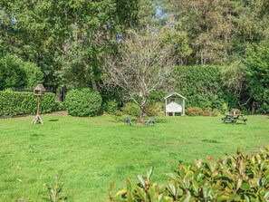 Un espace extérieur verdoyant avec un nichoir, un petit abri de jardin et une table de pique-nique.