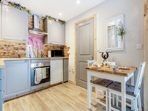 Een keuken met houten kastjes, een magnetron, een oven en een eettafel met stoelen.