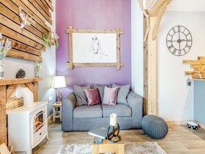 Een gezellige woonkamer met een grijze bank, een houten wand met een decoratie van een hertenhoofd, een schilderij van een paard in een lijst, een klok en een kleine witte verwarming.
