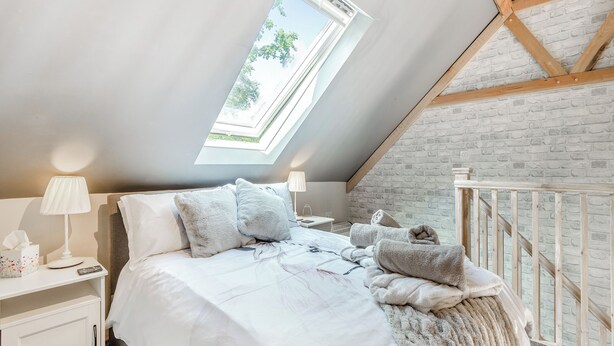 Une chambre avec un puits de lumière, un lit avec une literie blanche, une table de chevet, une lampe et un mur en briques.