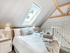 Un dormitorio con tragaluz, una cama con ropa de cama blanca, una mesita de noche, una lámpara y una pared de ladrillo.