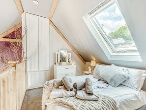 A bedroom with a skylight, a bed with towels, a nightstand, and a dresser.