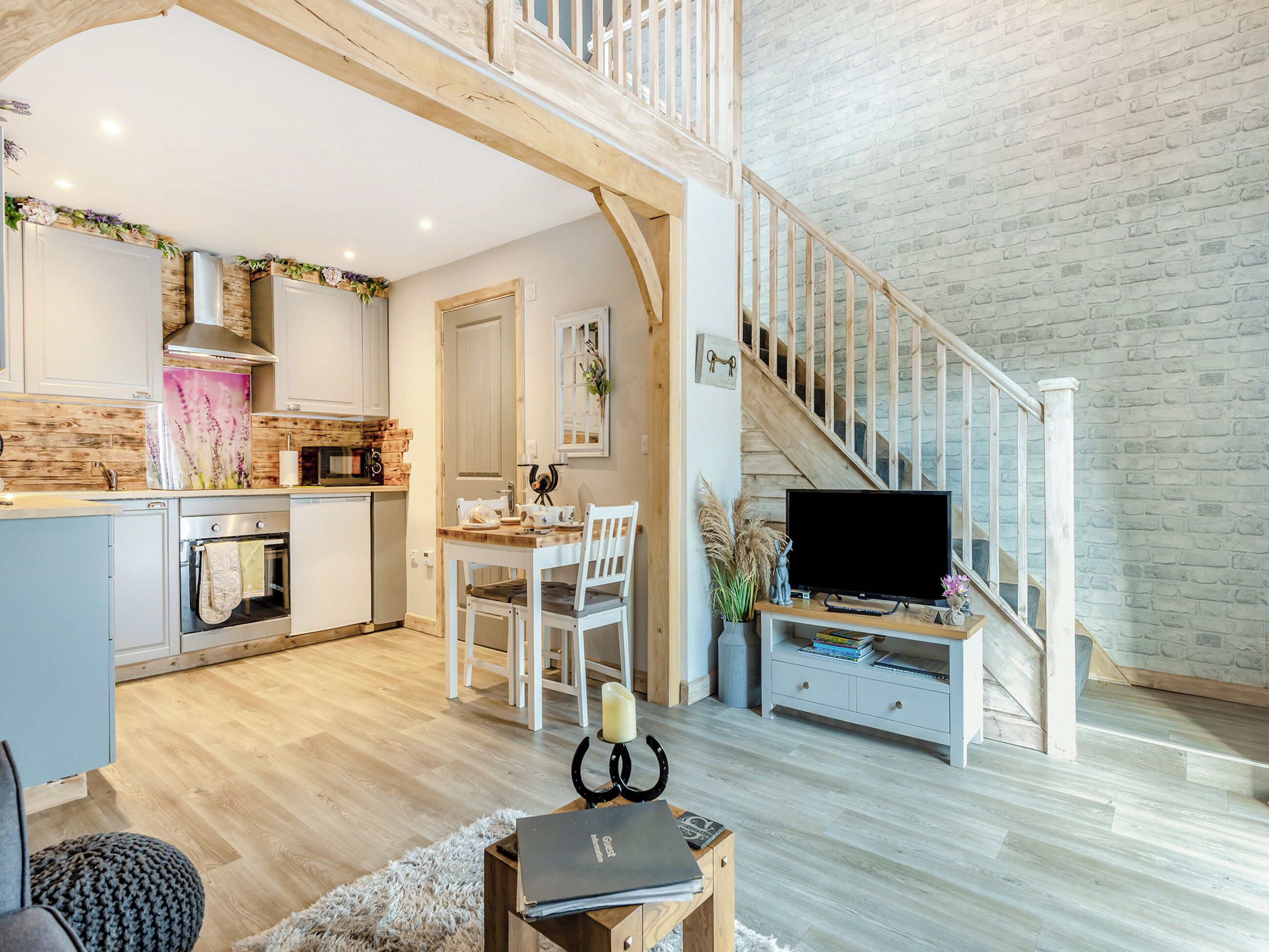 A spacious living area with a kitchen, dining table, and a staircase leading to an upper level.