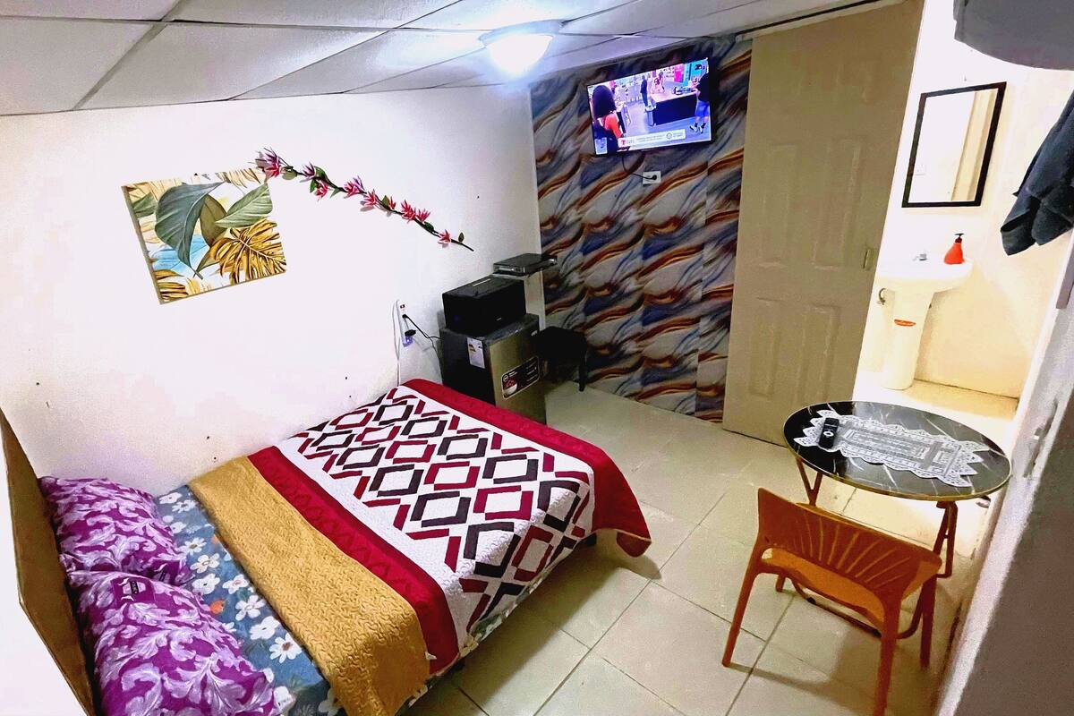 Una habitación de hotel pequeña con cama, escritorio, silla, televisor y baño.