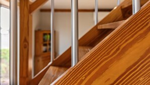 A wooden staircase with metal railings, leading to a room with a wooden cabinet and a window.