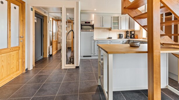 A modern kitchen with a wooden staircase, a central island, and a view of the living area.