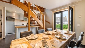 A modern kitchen with a wooden staircase, a dining area with a table set for four, and a view of the outdoors.