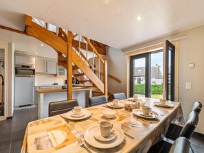 A modern kitchen with a wooden staircase, a dining area with a table set for four, and a view of the outdoors.