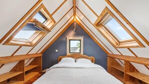 A bedroom with a sloped ceiling, wooden beams, a bed, and skylights.