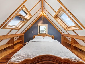 A bedroom with a sloped ceiling, wooden beams, a bed, and skylights.