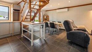 A modern kitchen with a wooden staircase, a dining area with chairs and a table, and a large window.