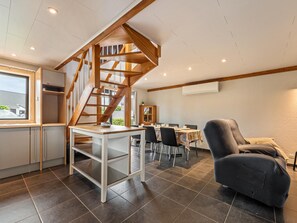 A modern kitchen with a wooden staircase, a dining area with chairs and a table, and a large window.