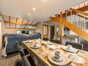 Un coin repas avec une table en bois dressée pour quatre personnes, un canapé et un escalier avec des rampes en bois.