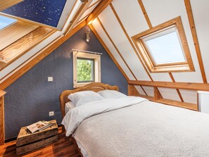 Una camera da letto con soffitto spiovente, travi in legno, un lucernario con motivo a stelle, una piccola finestra e una panca di legno con riviste.