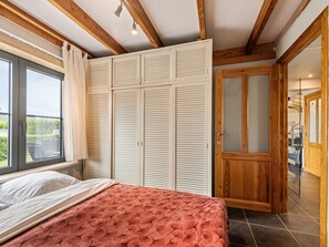 Une chambre à coucher avec un lit, une fenêtre avec des rideaux, une armoire et une porte en bois.