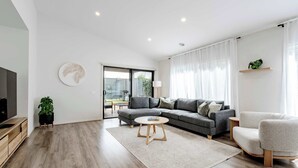 A modern living room with a grey sofa, a round coffee table, and a TV stand. - Coastal Family Retreat - Relaxed Living with Spa (Torquay)